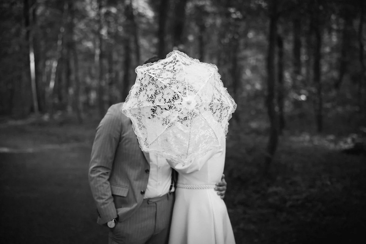 Brautpaar im Wald mit einem Blumenstrauß vor den Gesichtern
