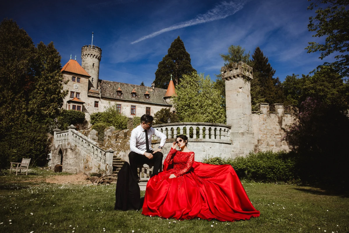 Paar mit rotem Kleid auf einer Wiese vor einem Schloss